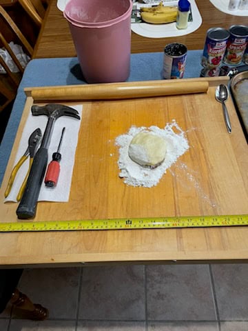 Dough on board with tools and ingredients nearby.