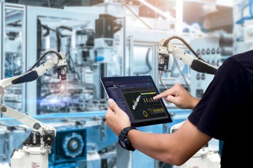 Engineer controls robotic arms with tablet in factory.